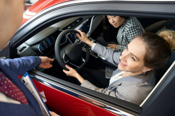 Two happy women in suits looking from automobile and direct their gaze at person