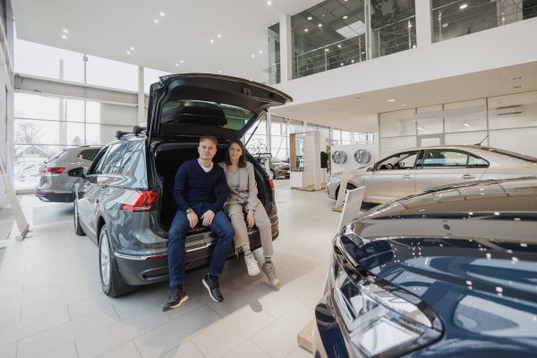 man buys a car at a car dealership. A female salesperson and car rental helps with the purchase. signing a trade-in contract and handing over keys, shaking hands. A successful man chooses a new car car. Car rental or repair service center.