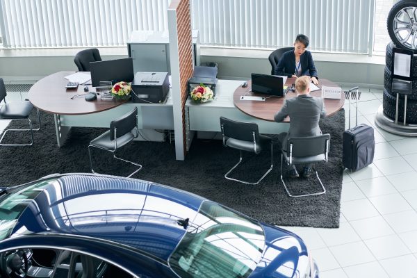 Young man with car dealer in auto show or salon